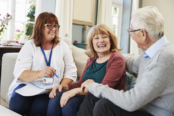 Senior living employee sitting with two residents on a couch.